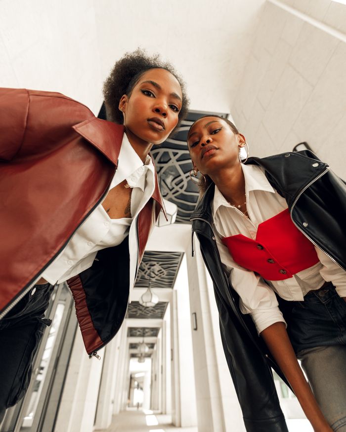 our-experience Two stylish women in modern attire pose confidently in an architectural corridor, showcasing bold fashion choices.