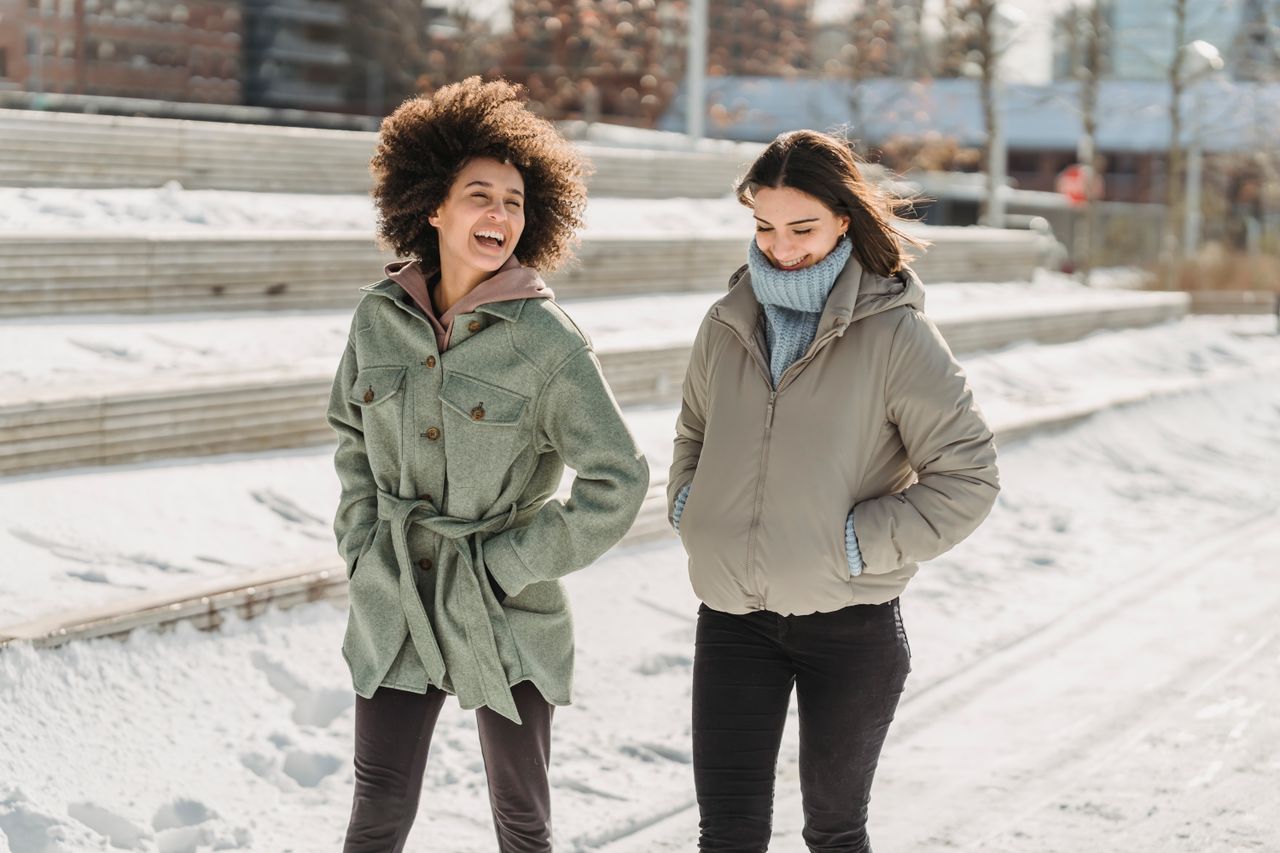 contact-img Expressive young multiracial female friends wearing warm clothes chatting and walking together with hands in pockets on snowy city street on freezing winter day
